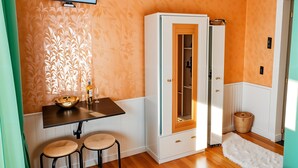 A room with a wooden cabinet, a small table with stools, a television mounted on the wall, and a patterned wallpaper. - cinecittaroomshaven (Rome)