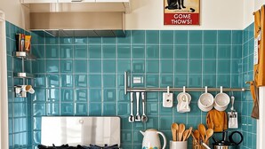 A kitchen with teal tiles, a stove, a refrigerator, and a hanging pot rack. - cinecittaroomshaven (Rome)