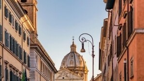 A street with historic buildings, including a prominent church with a dome and a bell tower. - cinecittaroomshaven (Rome)
