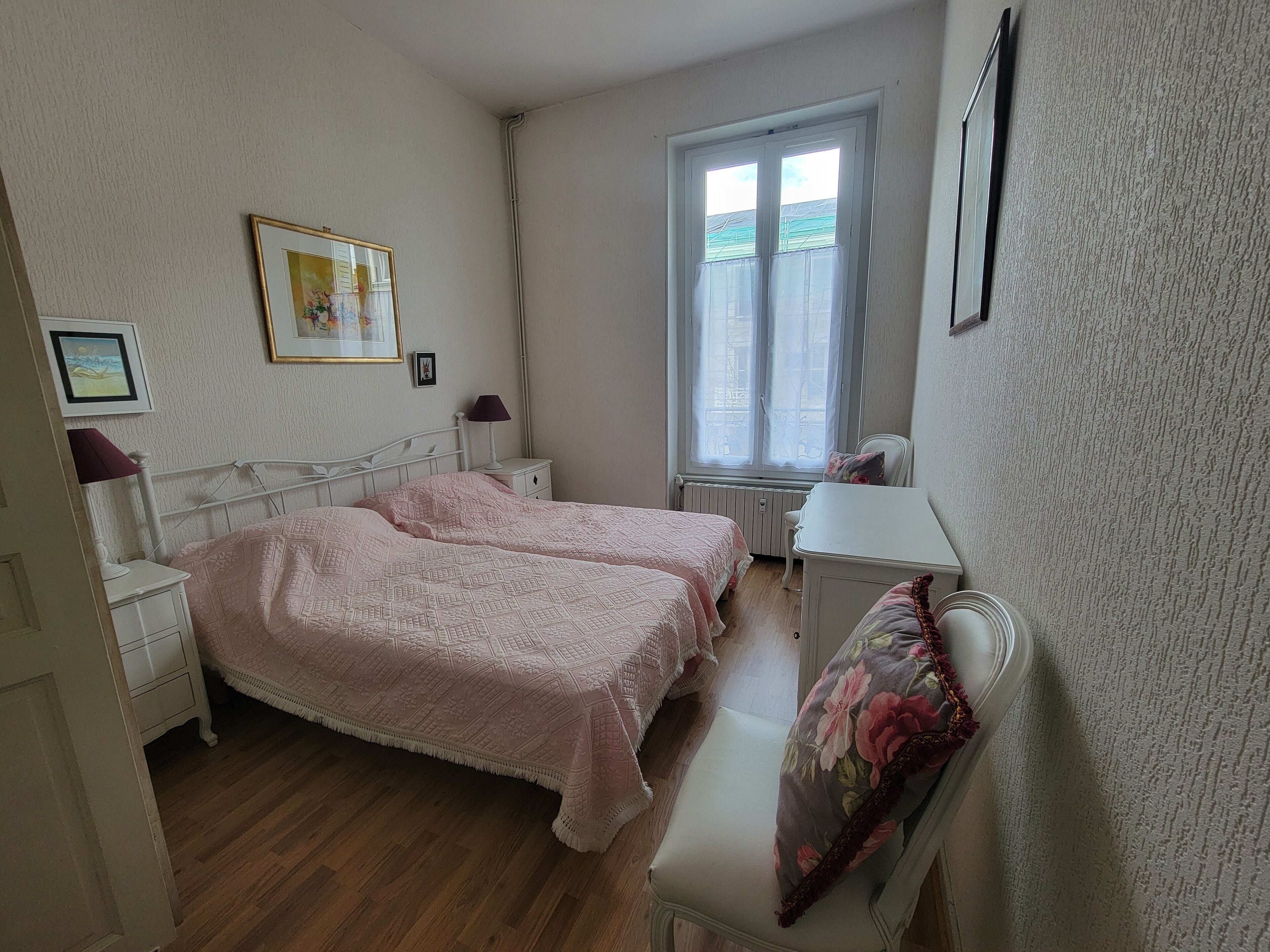 A bedroom with two beds, a window, a radiator, and a desk.