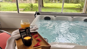 Een hottub met een houten dienblad waarop een kaars, een glas sinaasappelsap en een fles huidverzorging staan.