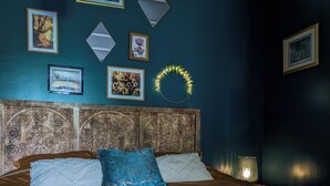 Een net opgemaakt bed met een dienblad vol ontbijt, waaronder gebak, een kom en een kopje, in een kamer met een donker blauwgroene wand, decoratieve spiegels en een gestreept hoofdeinde.