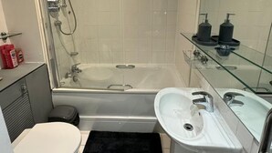 Egy modern fürőszoba üveg válaszfallal ellátott zuhanyzóval, fürdőkáddal, WC-vel és mosdókagylóval.