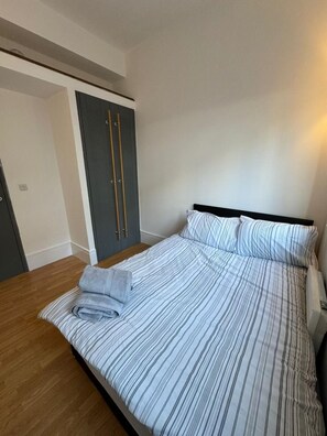 Un dormitorio con una cama, suelo de madera, un armario gris y una puerta.