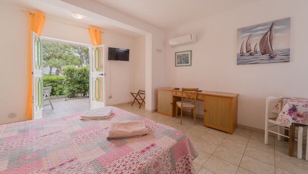 A bedroom with a bed, a desk, and a chair. There is a painting on the wall and an air conditioning unit. - Villino nel Bosco  (Capoliveri)