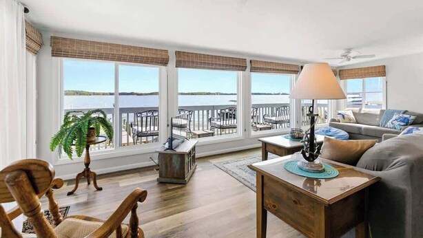 A spacious living room with large windows, a ceiling fan, and a view of the water. - Dolphins Chance - Waterfront Ocean Pines + Dock (Ocean Pines)