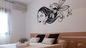 Un dormitorio con cama, almohadas, mesita de noche con lámpara y decoración en la pared.