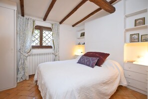 A bedroom with a bed, a window with curtains, a bedside table with a lamp, and a dresser.