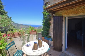 A round table with two decorative vases and a chair, set against a scenic backdrop with a clear view of the sea and hills.