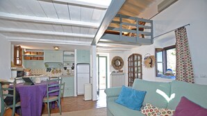 Un salon confortable avec un canapé, une table à manger avec des chaises, un coin cuisine avec des placards et un réfrigérateur, et un espace en mezzanine situé au-dessus.