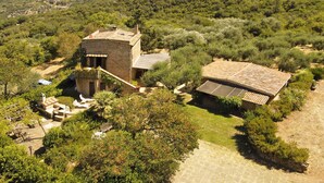 Un bâtiment en pierre, doté d’un toit en tuiles, entouré d’une végétation luxuriante et situé dans un paysage vallonné.