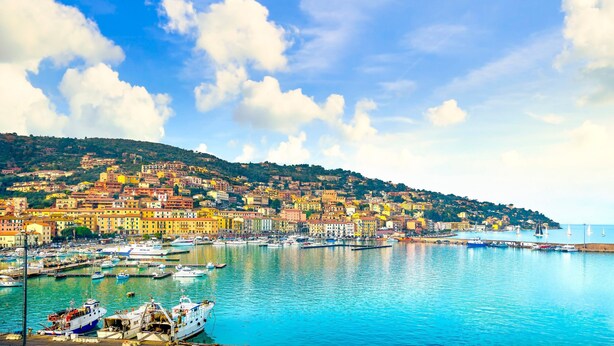 Une ville côtière aux bâtiments aux couleurs vives, un port de plaisance rempli de bateaux et un ciel d’un bleu limpide.