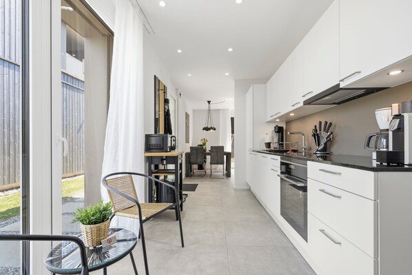 A modern kitchen with white cabinets, a built-in oven, and a coffee machine.