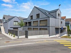 A modern building with a grey facade, multiple windows, and a visible entrance.