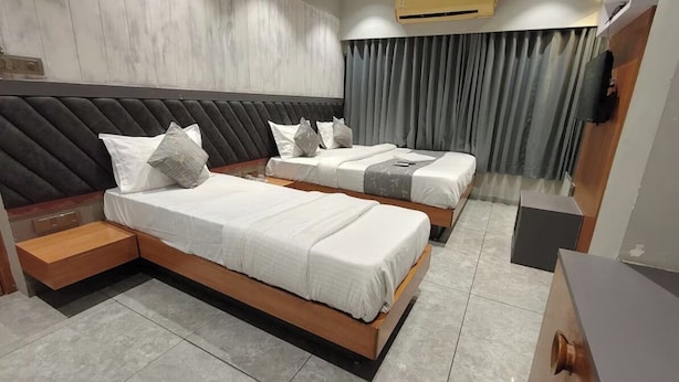 Quarto de hotel com duas camas, cabeceira de madeira, TV de tela plana e cortina cinza.