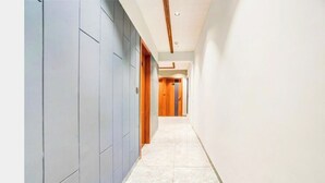 Um corredor com armários cinzas em um lado, uma porta de madeira no final e piso de azulejos.
