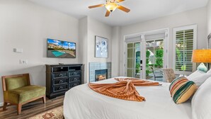 A hotel room with a bed, a television, a fireplace, and a view of the outdoors through the door. - LV033 Quaint Downstairs Legacy Villas Suite (La Quinta)