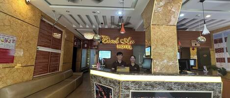A hotel reception area with a marble counter, a reception desk, and a large illuminated sign above.