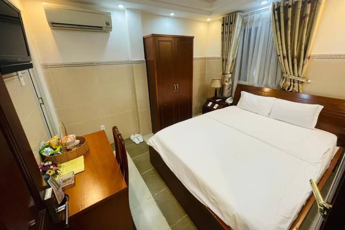 Una camera d'albergo con un letto grande, un armadio in legno, un tavolino con un cesto e ciabatte, e un condizionatore d'aria.