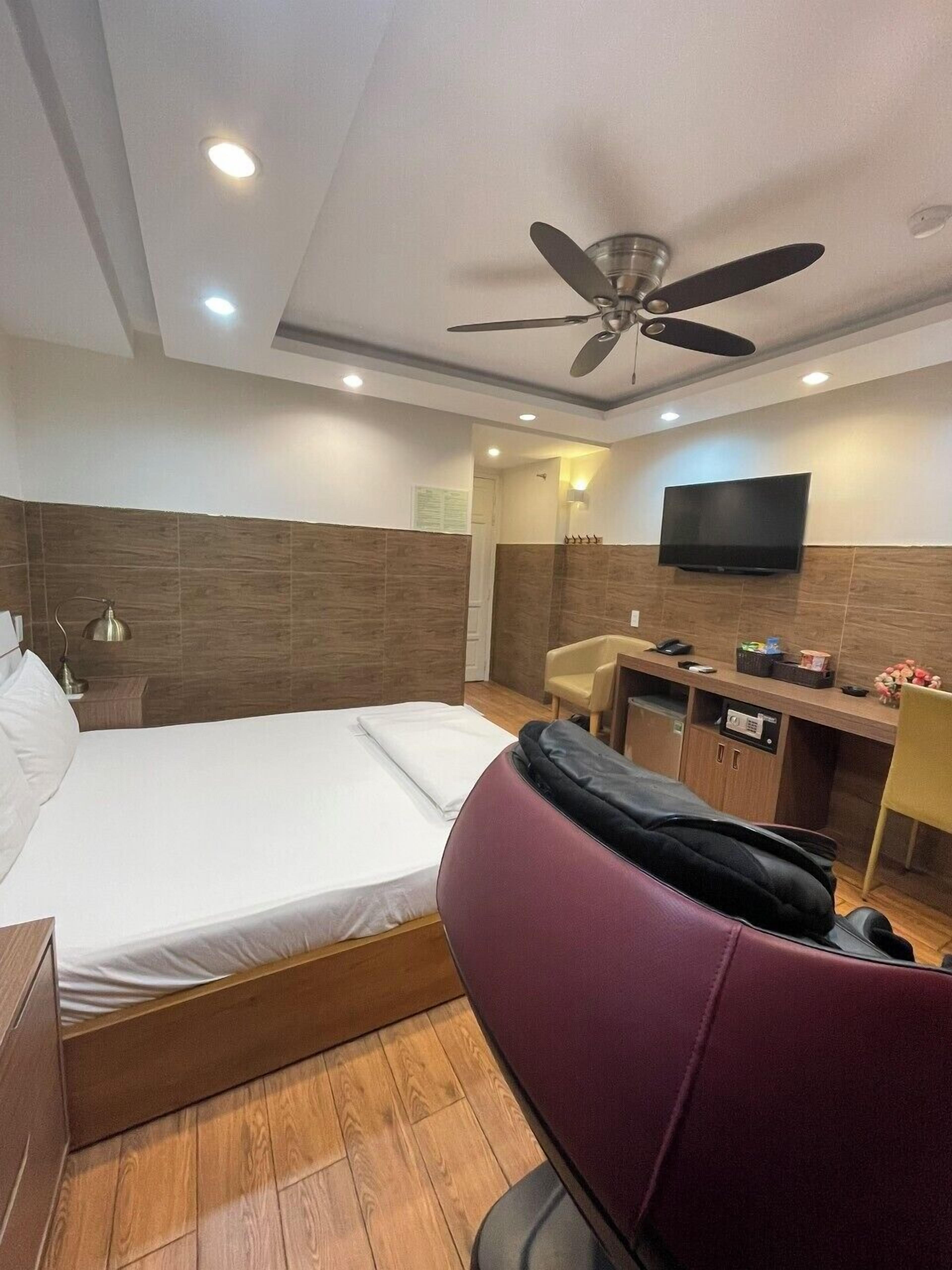 Una habitación de hotel con cama, escritorio, silla, televisor y ventilador de techo.