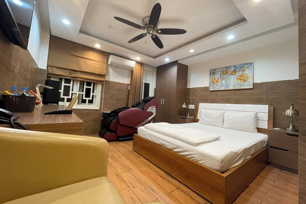Camera d'albergo moderna con un letto grande, una poltrona massaggiante, una scrivania con telefono e una ventola a soffitto.