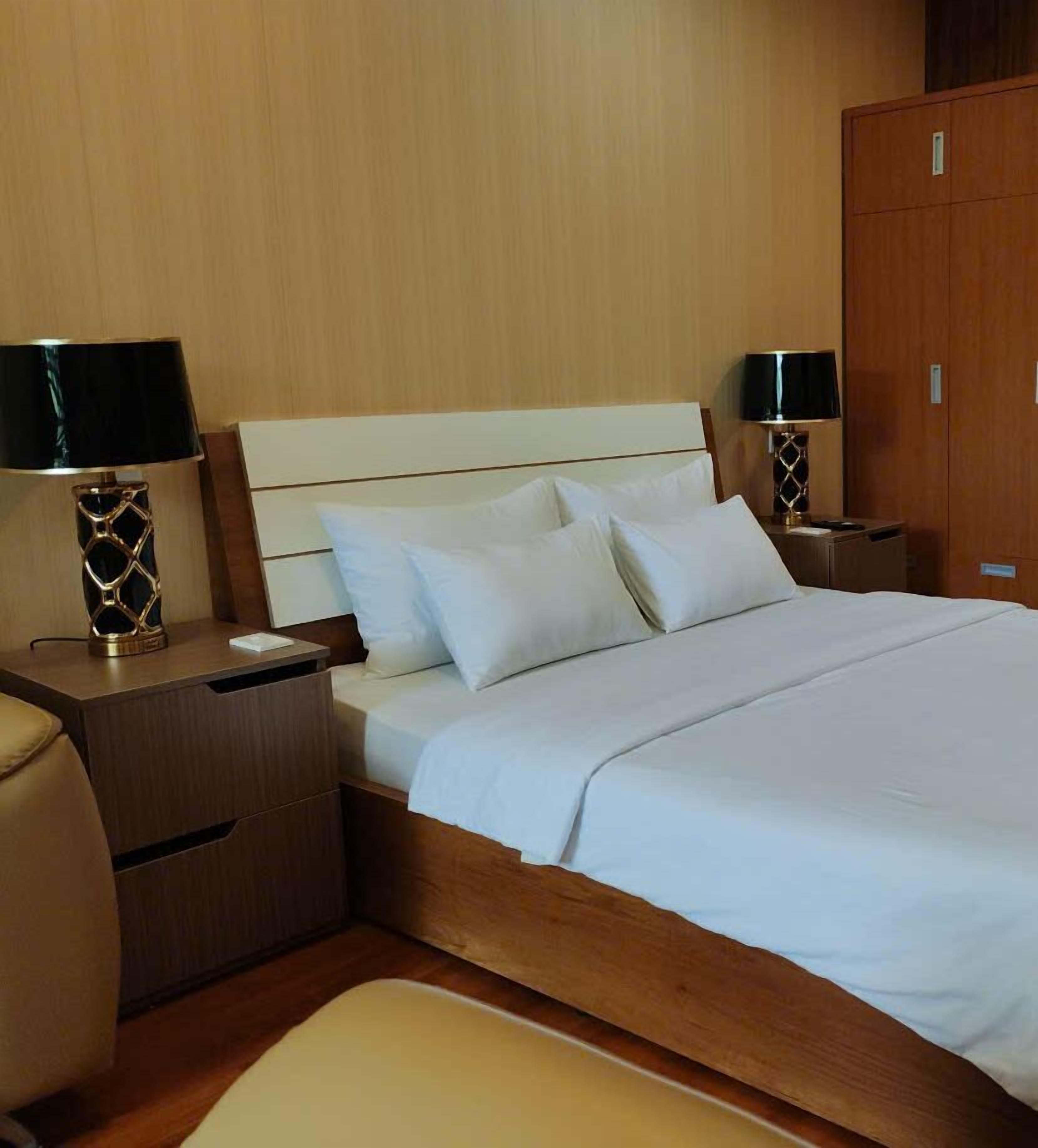 A hotel room with a bed, two nightstands, a wooden wardrobe, and a chair.