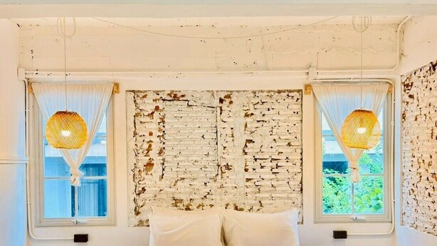 Un dormitorio con una cama, dos ventanas con cortinas, una pared con textura y una alfombra estampada.