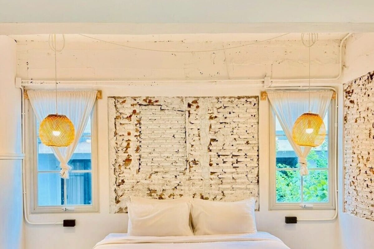 A bedroom with a bed, two windows with curtains, a textured wall, and a patterned rug.