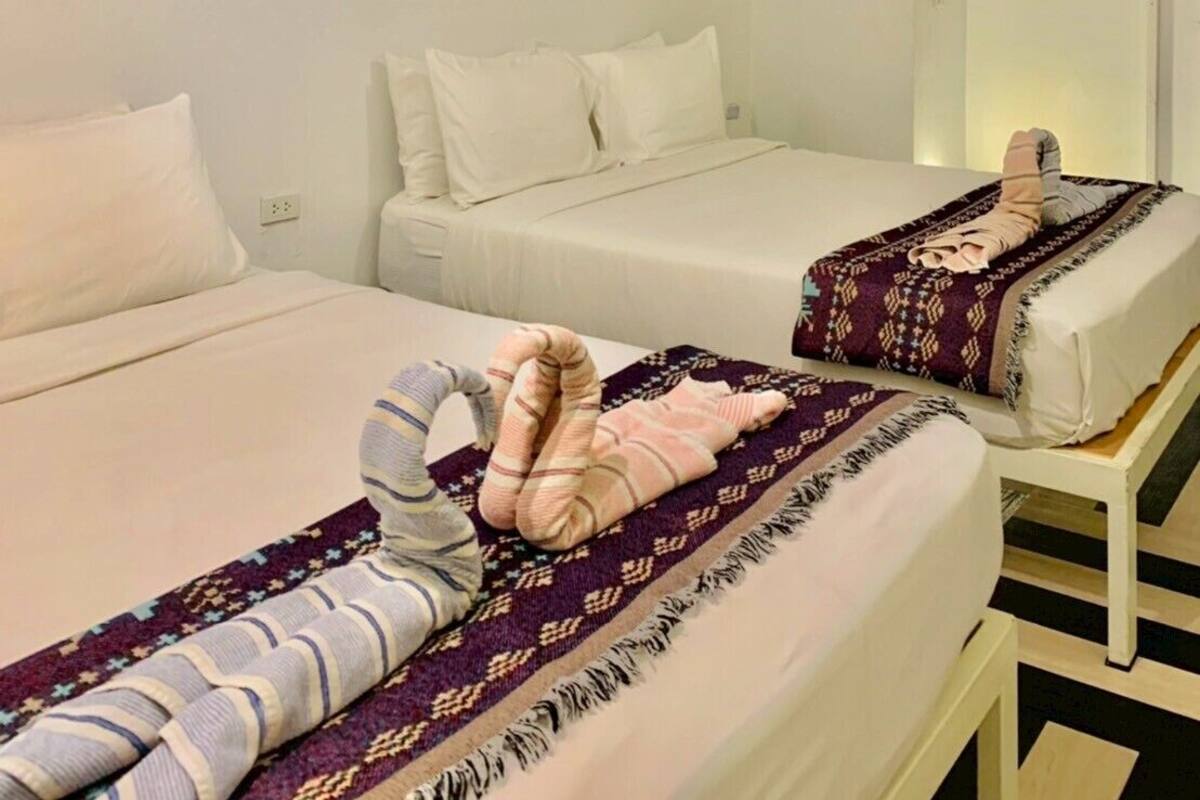 A hotel room with two beds, each with a patterned blanket and a rolled-up towel.