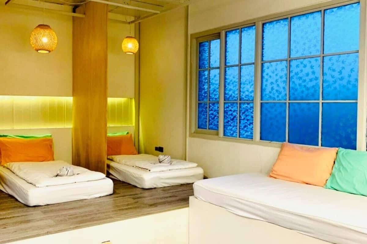 A room with a bed, a window with blue patterned blinds, and a wooden floor.