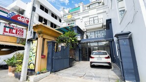 Una entrada cerrada con portón a un edificio, un automóvil estacionado, un cartel de restaurante coreano y un letrero de casa.