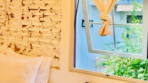 Una habitación con pared de ladrillo blanco, ventana con cortina recogida y lámpara colgante tejida.