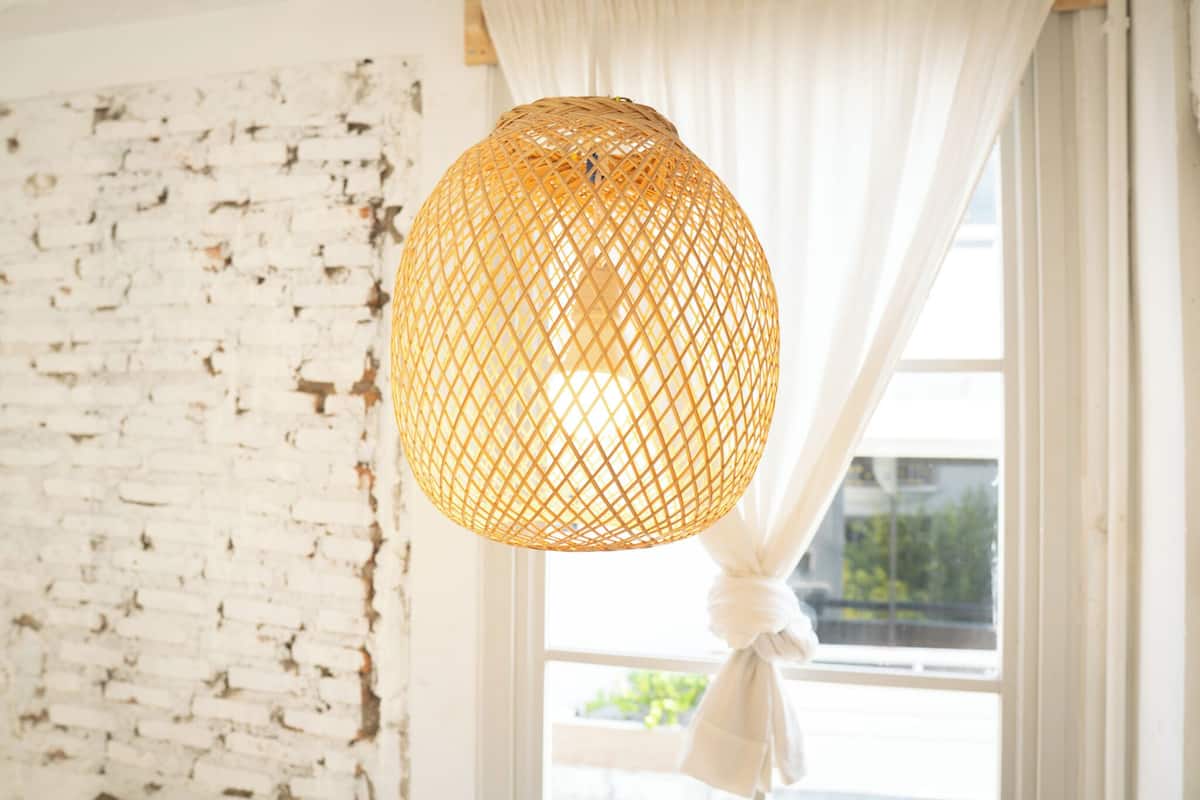 A room with a white brick wall, a window with white curtains tied back, and a hanging woven light fixture.