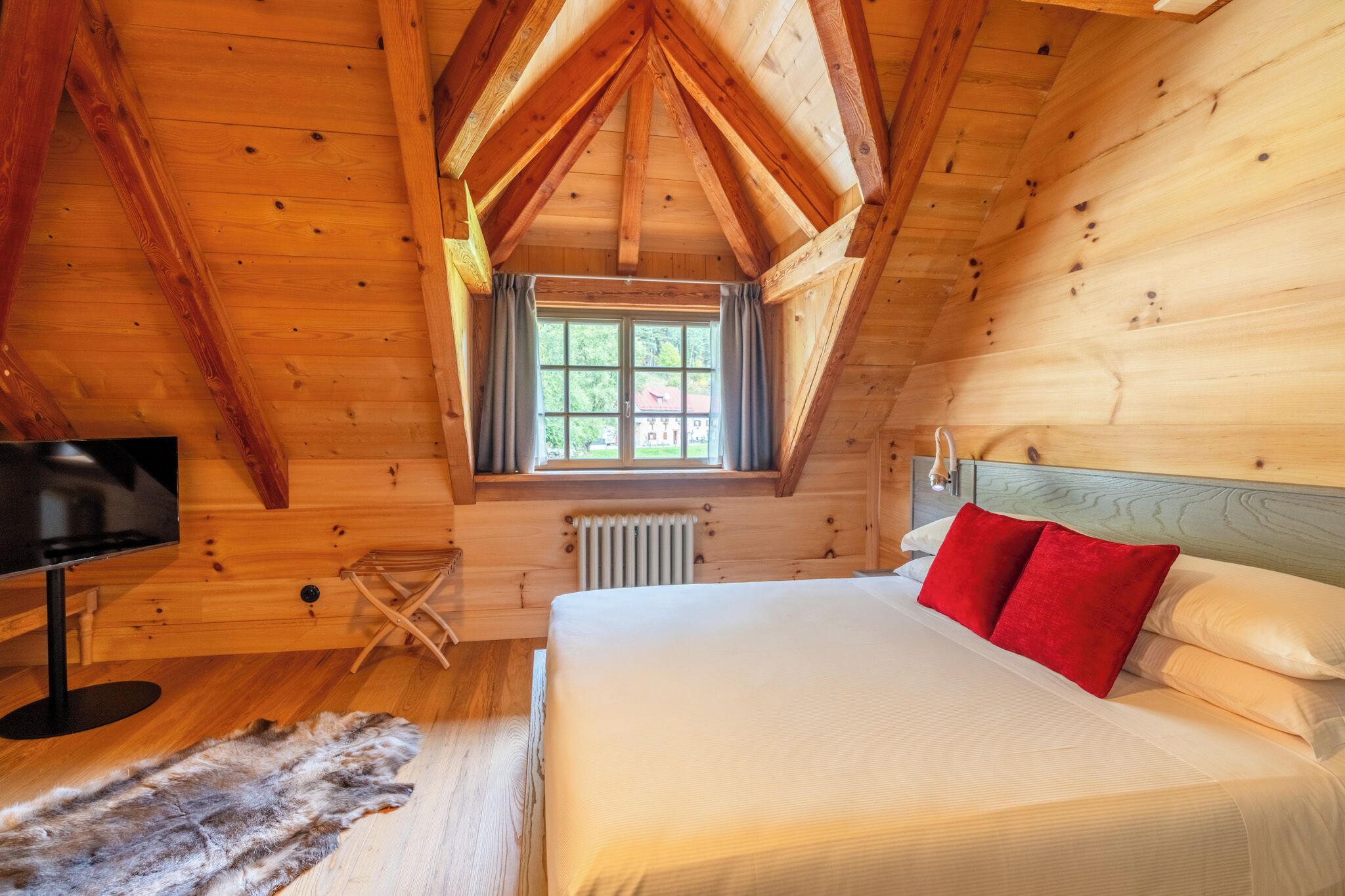 A wooden cabin bedroom with a bed, a window, a radiator, and a television.