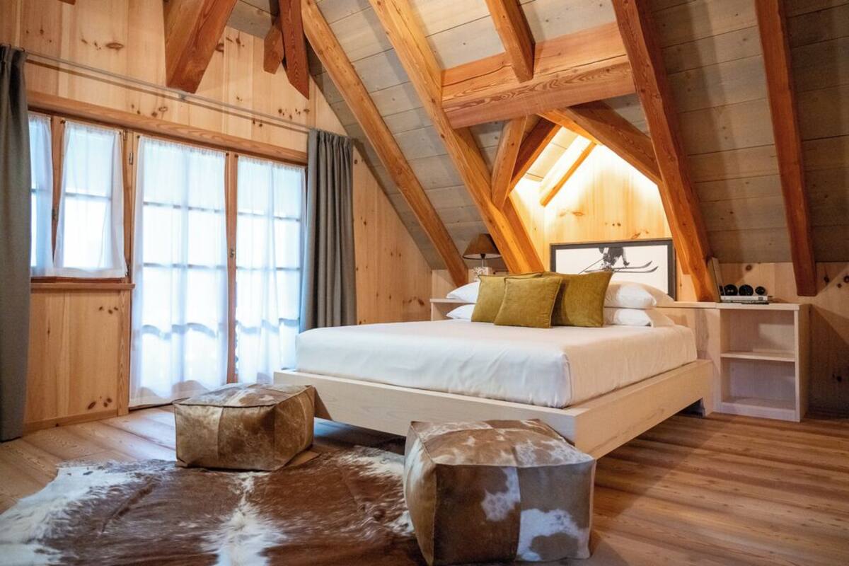 Une chambre mansardée en bois, avec un lit, deux poufs et un tapis en peau de vache.