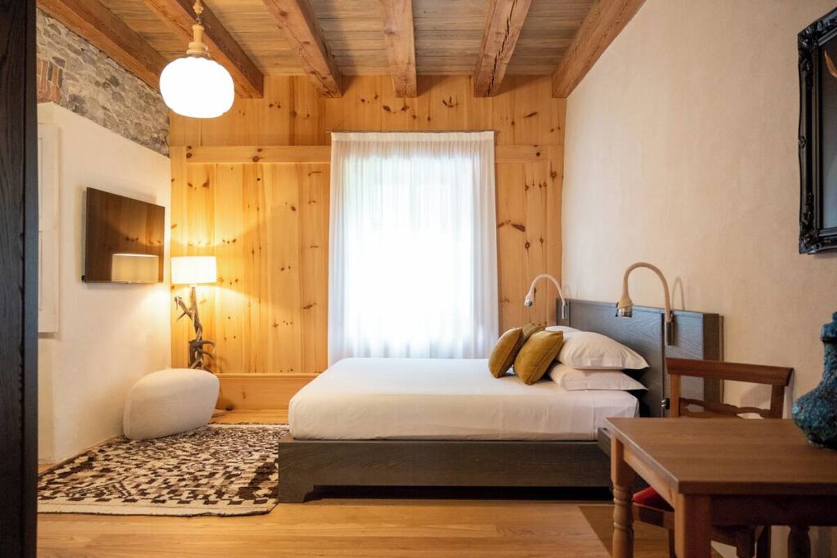 Une chambre à coucher aux murs lambrissés, avec un lit, une table de chevet, une lampe et une vue sur l’extérieur par une fenêtre.