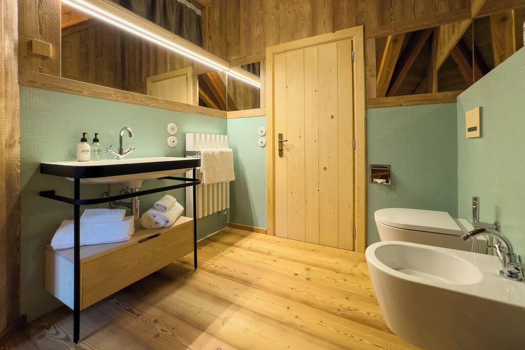 Une salle de bain au sol en bois, dotée d’un grand lavabo, d’un miroir et d’un porte-serviettes.