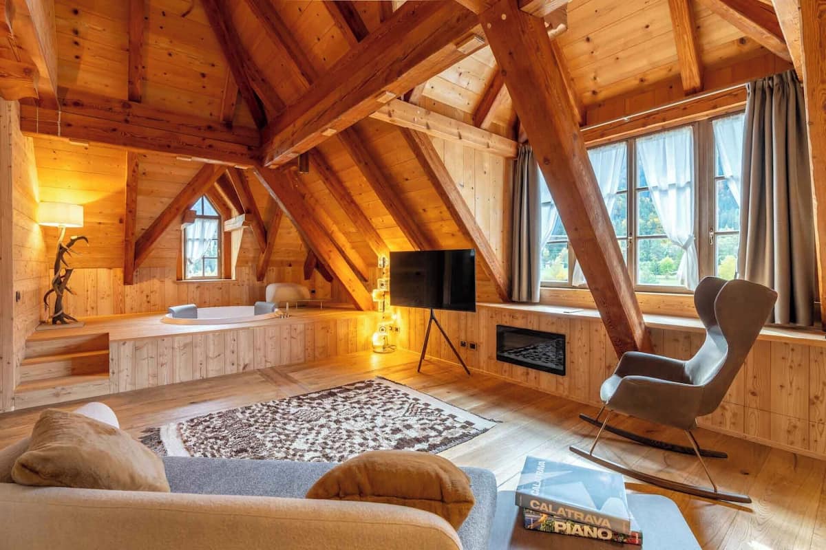 L’intérieur d’un chalet confortable, avec un plafond en bois, une grande fenêtre, une cheminée, un téléviseur et un canapé.