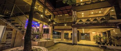 Un edificio de varios pisos con un patio, zona de estar al aire libre y un árbol en el centro.