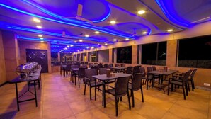 A restaurant with a long counter, multiple tables, and chairs. - Amansaraa Bhide Retreat (Alibag)