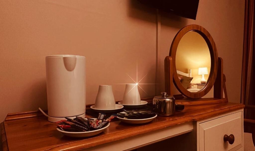 Une chambre d’hôtel avec une commode en bois, une grande machine à café blanche, un miroir et une assiette de collations.