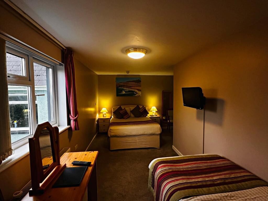 A compact hotel room with a single bed, a desk with a chair, a television, and a window with curtains.