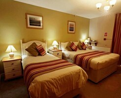 A hotel room with two beds, each with a bedside table and lamp, and a large window with a view.