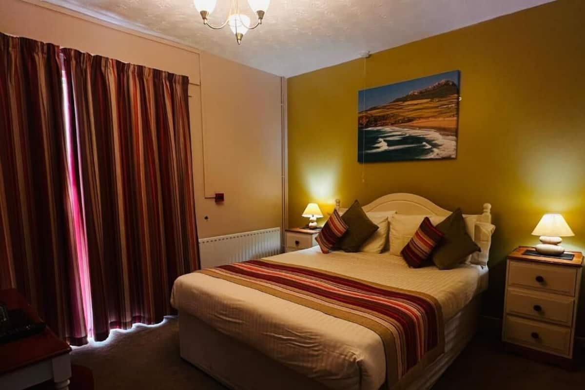 Une chambre à coucher avec un lit, des tables de chevet, une lampe, un tableau au mur et des rideaux.