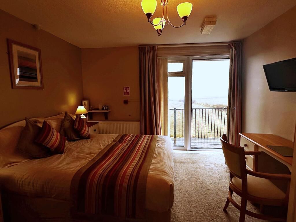Een hotelkamer met een bed, een bureau, een stoel, een televisie en een balkon met uitzicht.
