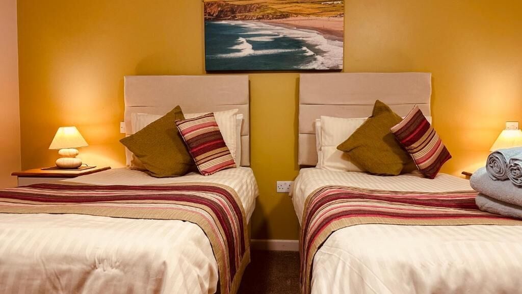 Habitación de hotel con dos camas, cada una con ropa de cama y almohadas a rayas, un cuadro de una playa sobre las camas, y una lámpara a cada lado de las camas.