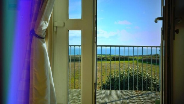 Een balkon met een metalen hekwerk met uitzicht op een grasveld en een heldere lucht.