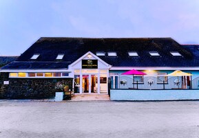 Un hotel con fachada de piedra, un amplio acceso y un área exterior cubierta con sombrillas.