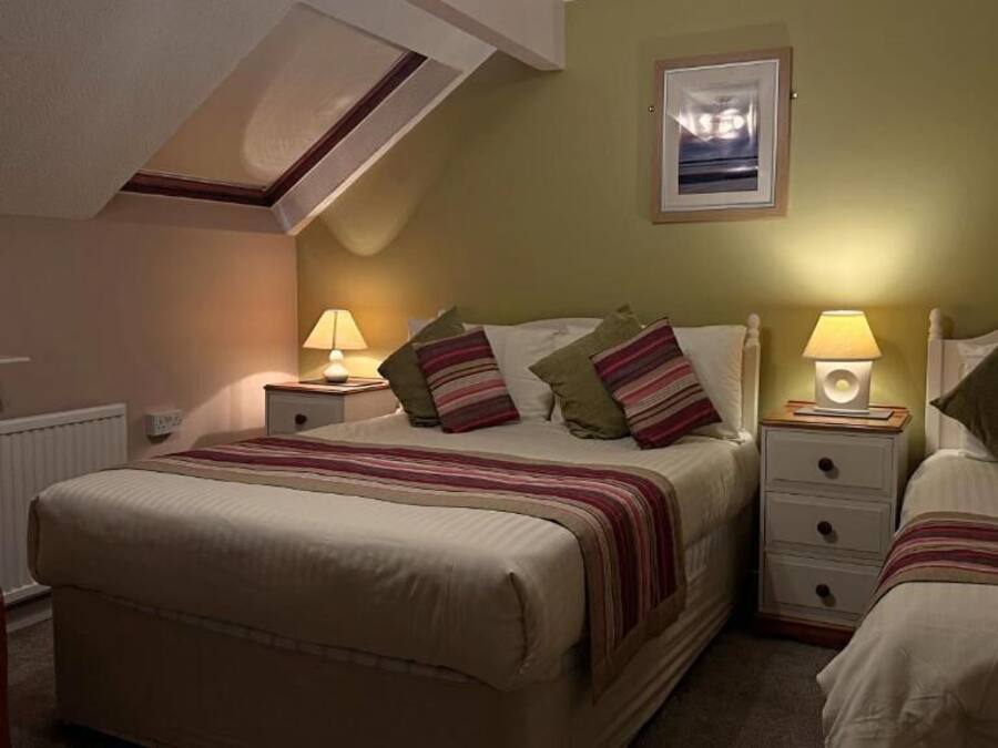 Quarto de hotel com uma cama grande, duas mesas de cabeceira com abajures, uma cadeira e um quadro na parede.