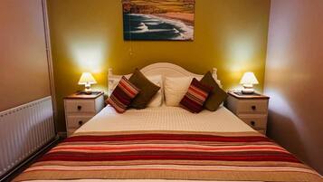 A bed with a striped bedspread, two bedside lamps, and a painting of a coastal landscape on the wall.